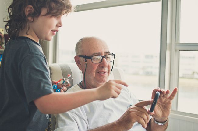 Een grootouder en kleinkind communiceren met een smartphone terwijl het kind een kleine robot vasthoudt.