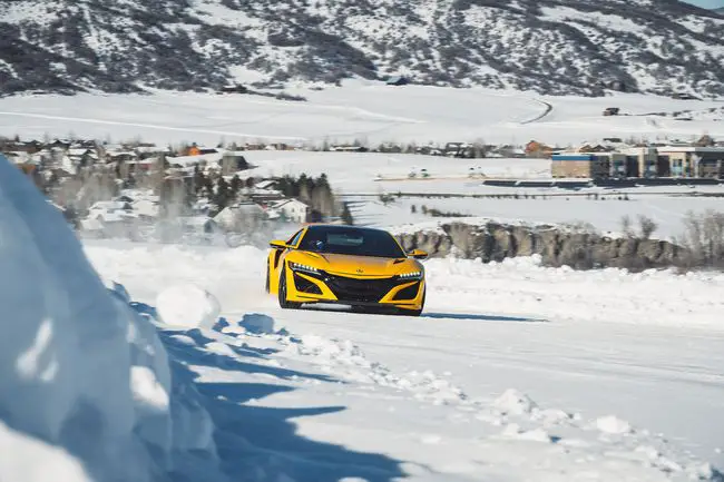 Een gele Bridgestone-testauto die op een besneeuwd parcours rijdt om de tractie van de banden te testen.