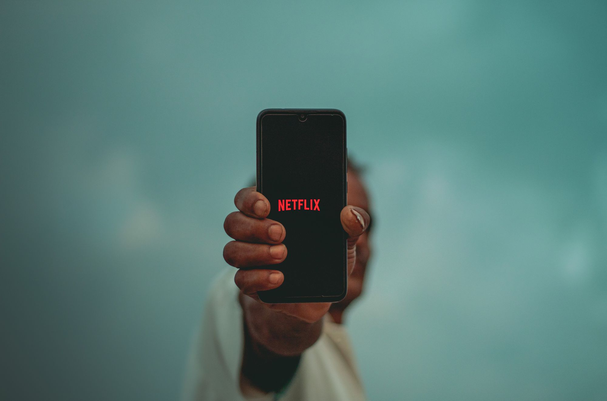 Een persoon die een zwarte iPhone op armlengte houdt met het Netflix-logo op het scherm. 