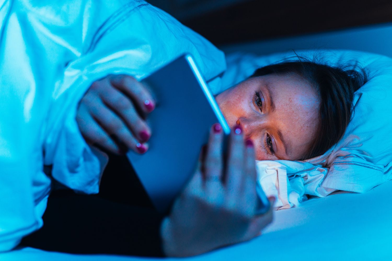 vrouw die haar tablet 's nachts in bed gebruikt